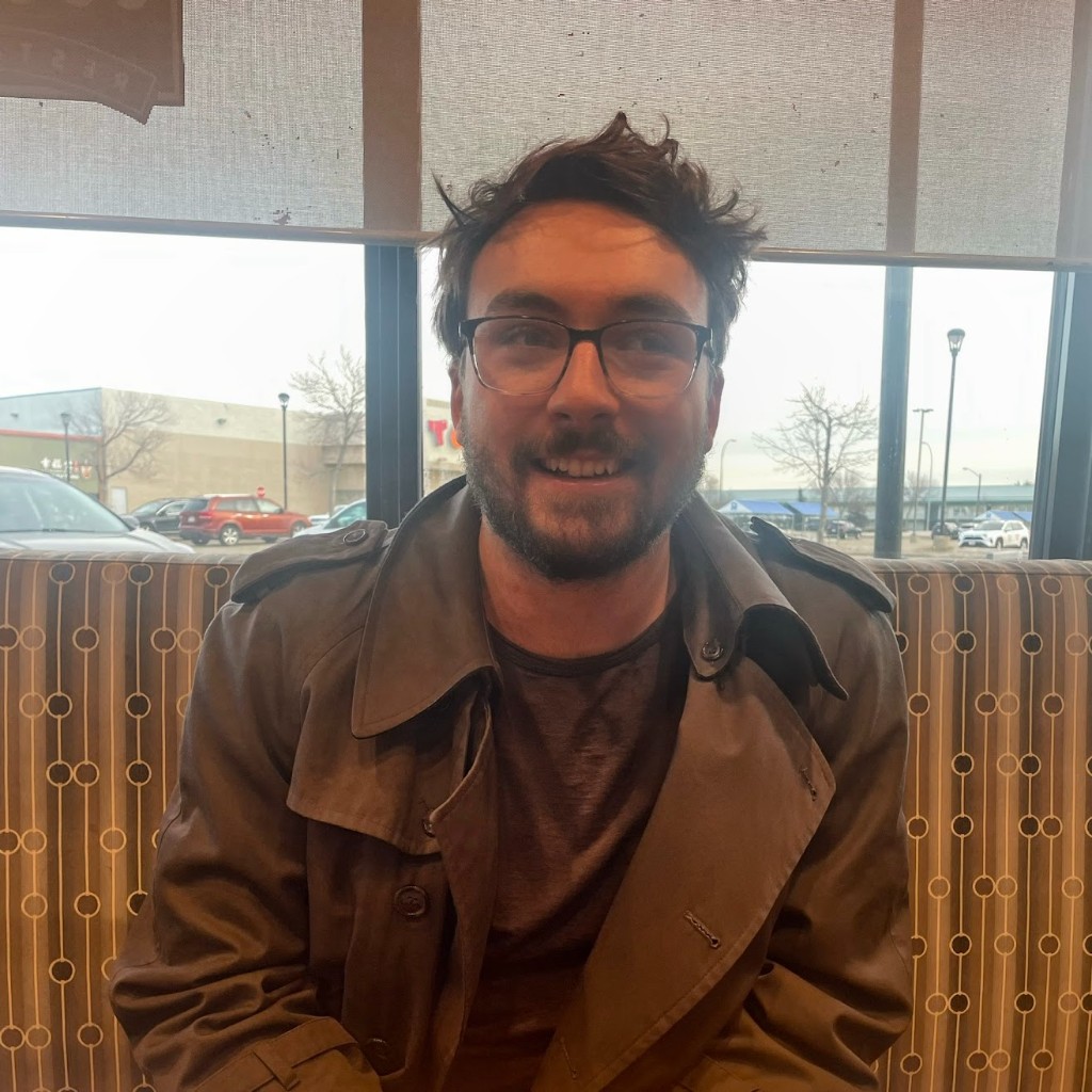 Isaac smiling, seated in a restaurant booth by a window