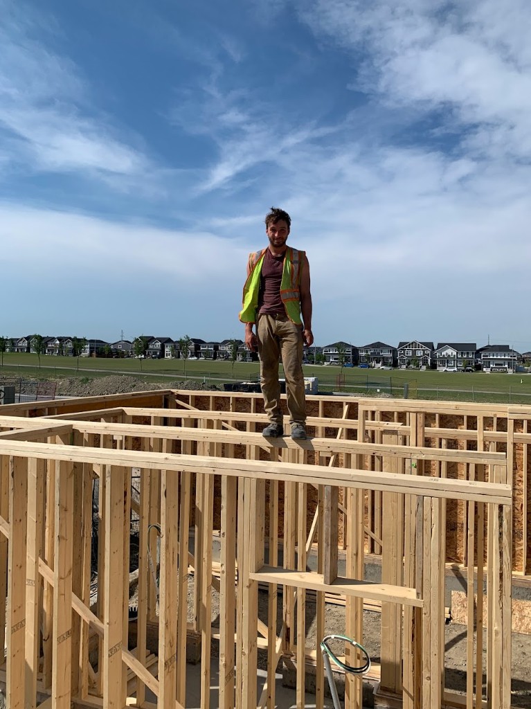 Isaac in a high-visibility vest standing on wall framing at a residential build site